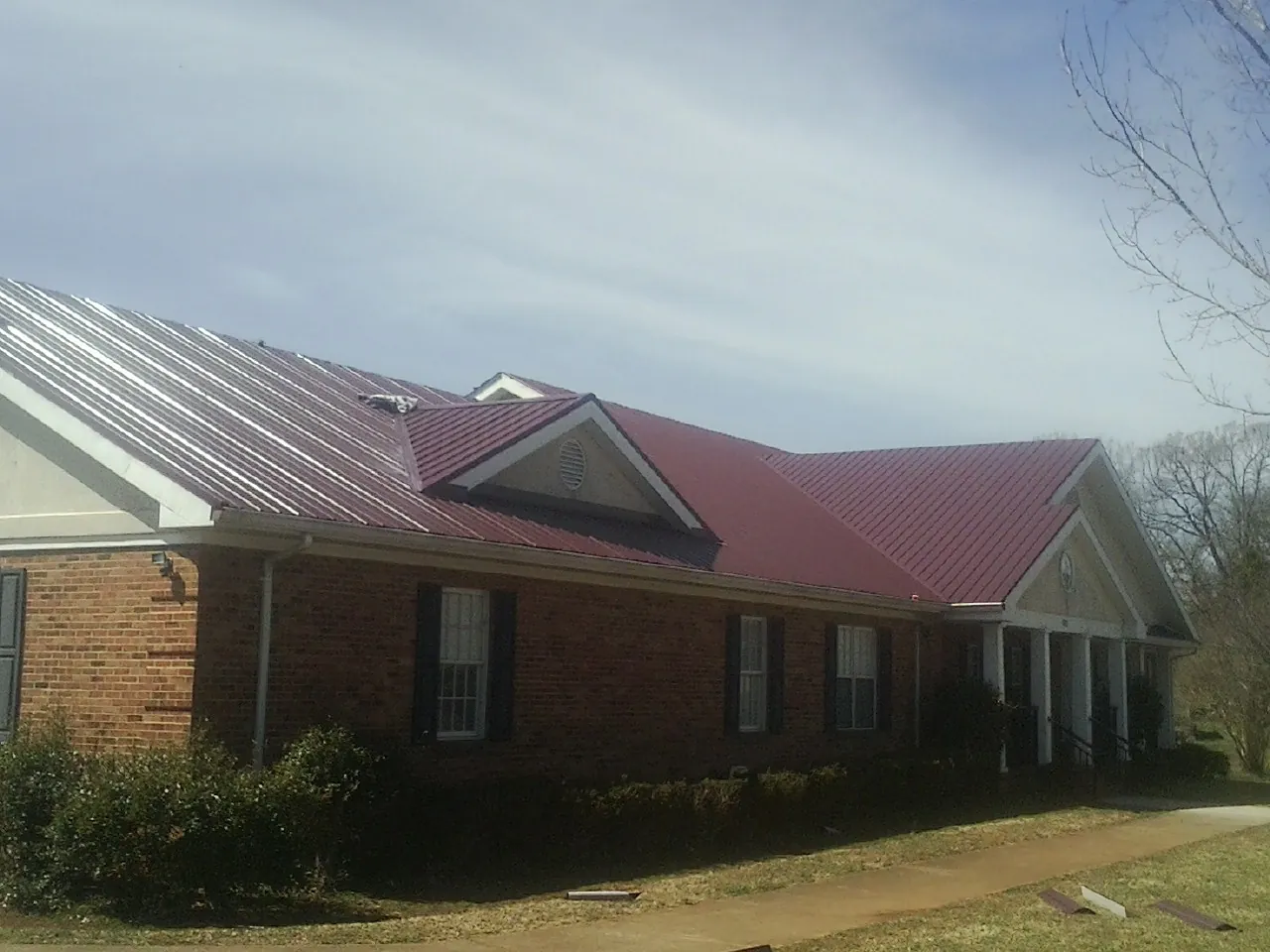 Red metal roof with gabled entries on a long brick building, from a Hail Damage Roof Repair job in Lapwai