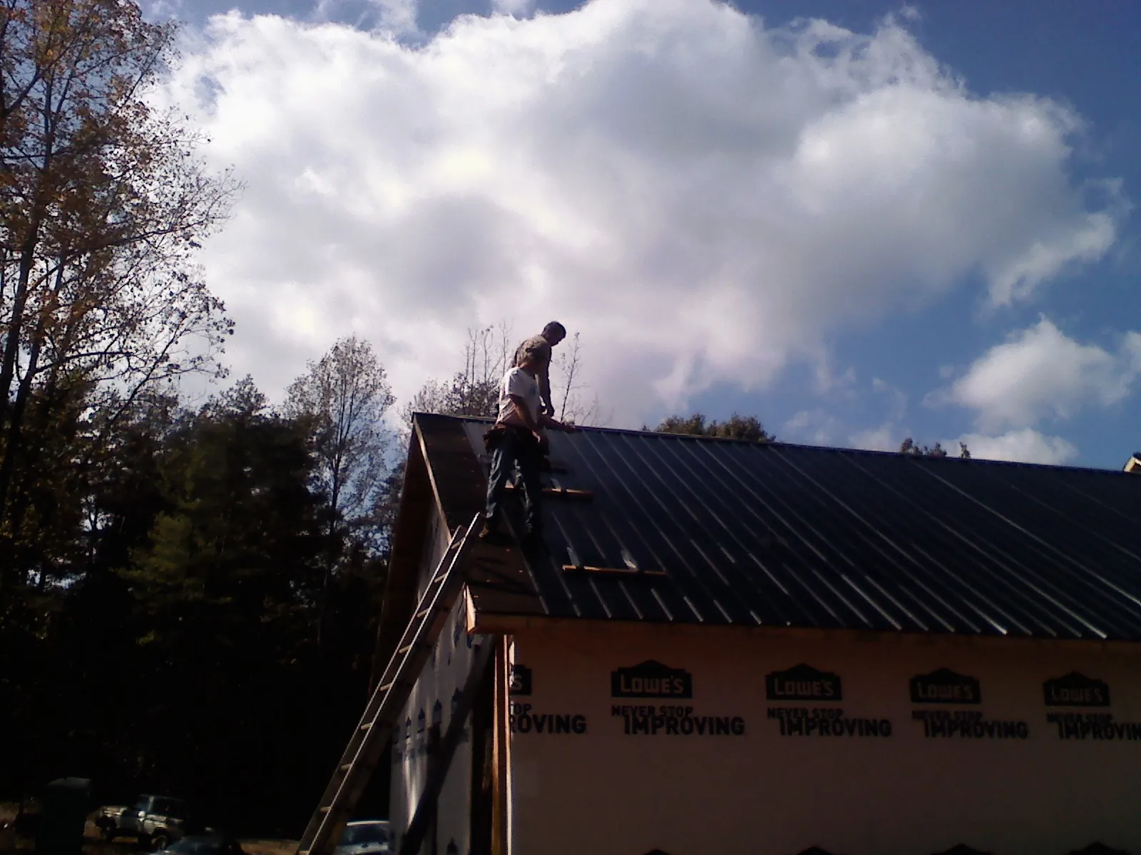 Roofer fastening dark metal panels high against a cloudy sky, from a Roof Inspection job in Lapwai