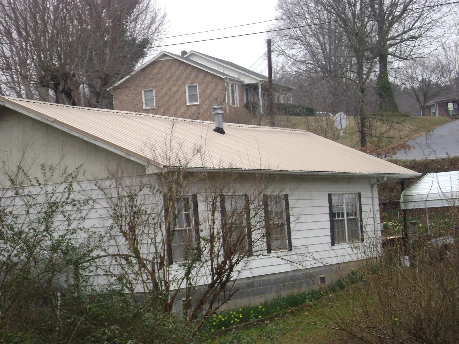 Tan metal roof on a white sided house set into a hillside — Commercial Roofing by Roofing Brothers in Lapwai